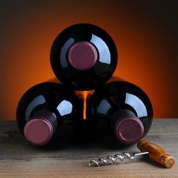 Three wine bottles and antique cork screw on a rustic table with warm background. Square Format.
