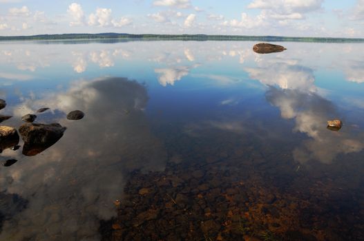 The bottom of the lake with a lot of stones and reflected sky