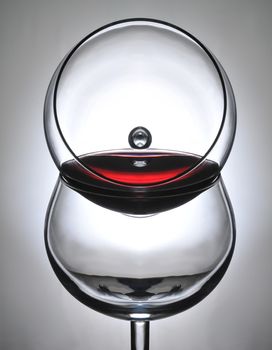 Closeup of a wine glass resting on the bowl of a second wineglass with a light to dark spot backlight. The top glass is partially filled with red wine.