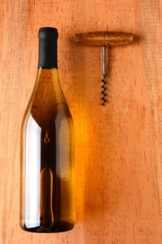 A chardonnay wine bottle and corkscrew on a rustic wood surface. The bottle has no label and there is plenty of room for your copy.