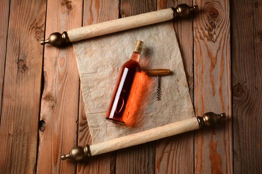 A bottle of blush wine and corkscrew laying on a scroll of parchment paper on a rustic wooden floor.