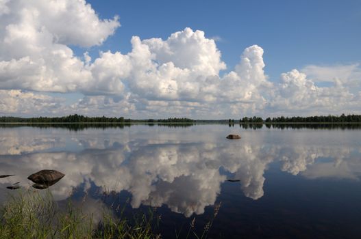 The picture shows typical landscape in the south region of Karelia - blue sky, clouds, big lake looks like a mirror and a lot of distant green islands, trees, stones and rocks