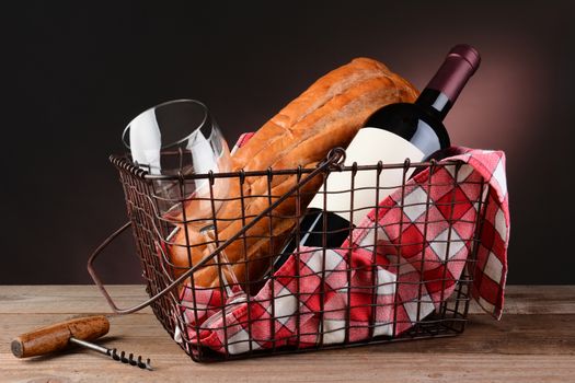 Wine and bread in wire picnic basket on a rustic wood table with warm light to dark background. Horizontal format. 