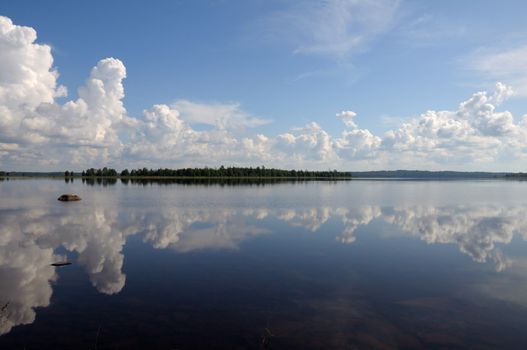 The picture shows typical landscape in the south region of Karelia - blue sky, clouds, big lake looks like a mirror and a lot of distant green islands, trees, stones and rocks