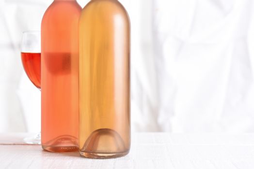 Wine Still Life: High key wine bottles on a white wood table in front of a window.