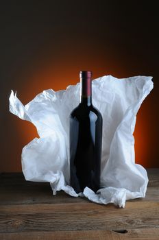 Red Wine Bottle with tissue paper wrapping on wood surface and light to dark warm background.