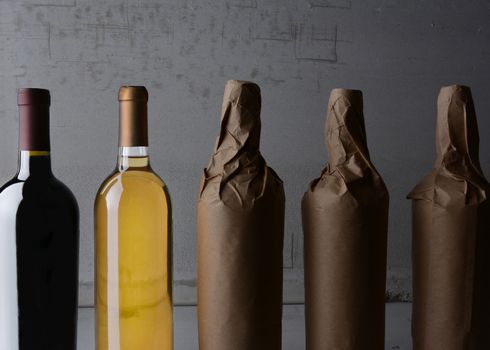 Five Wine Bottles, three wrapped in plain paper with one red wine and one white. Strong side light with copy space. 