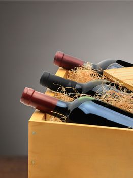 Three bottles of red wine in a wood crate with a light to dark gray background.