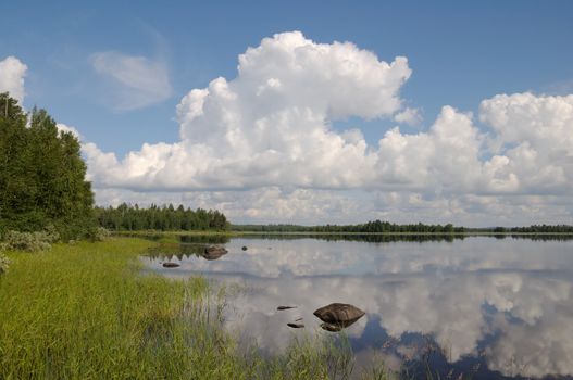 The beautiful picture of Karelian forest at the edge of a lake, and some huge boulder in this lake