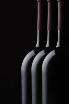 Low Key Wine Bottle Still Life: Closeup of three red wine bottles against a black background, with copy space.