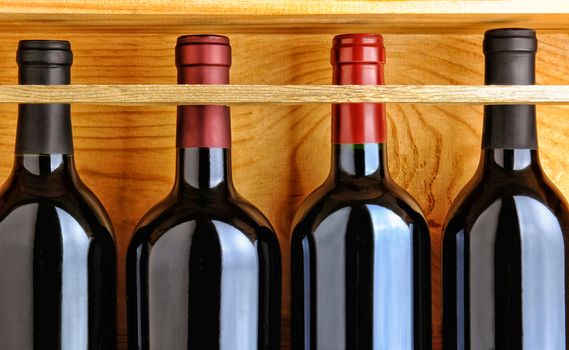 Four red wine bottles in a wooden case. Closeup filling the frame.