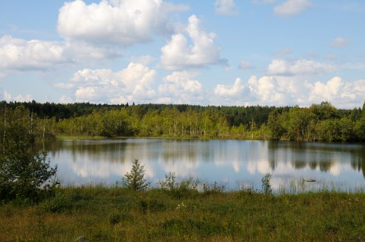 Beautiful lake in a forest under blu sky with cumulus clouds