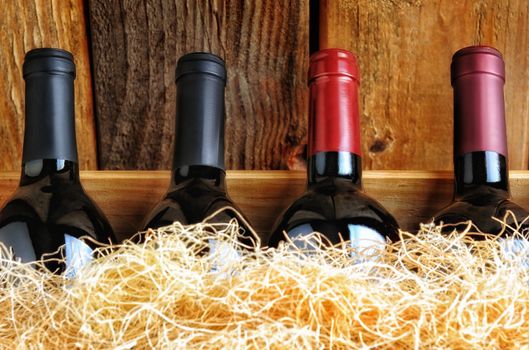 Closeup of four different wine bottles in a wooden crate with straw packing material.