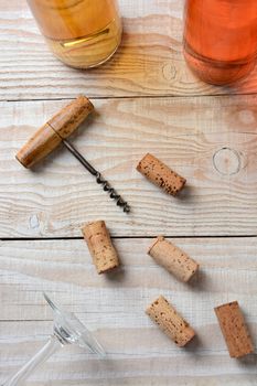 Vertical high angle closeup of an old fashioned corkscrew on a table with random corks two wine bottles and a wine glass bottom.