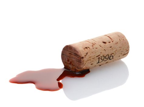 Closeup of a wine cork and a wine spill on white with reflection. Horizontal format.