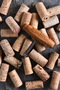 An antique corkscrew laying on a group of corks. Vertical format shot from a high angle.