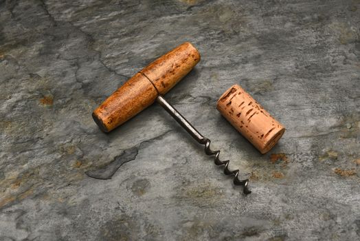 Top view of an old fashioned cork screw and cork on a slate background.