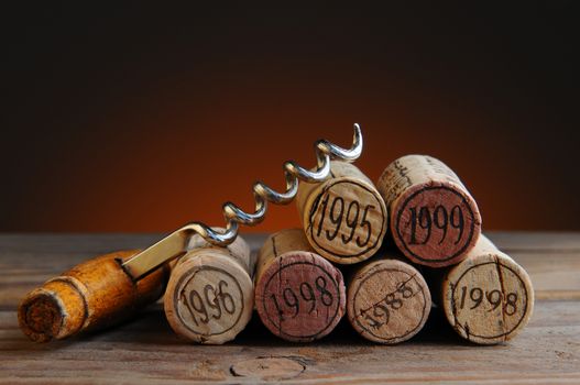 Closeup of a group of wine corks and a corkscrew on a rustic wood table and a light to dark warm background.
