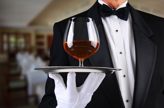 Closeup of a waiter in a restaurant with a brandy snifter on a serving tray. 
