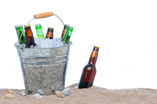 Assorted beer bottles in a bucket of ice in the sand isolated on white. One beer bottle without a cap is by itself stuck in the sand next to the pail.