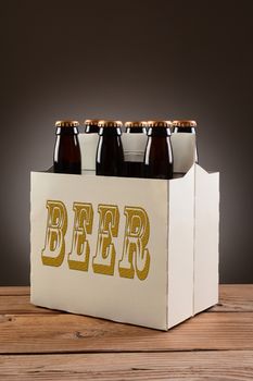 Closeup of a six pack of brown beer bottles with the word BEER written on the side, sitting on a rustic wooden table. Vertical format with a light to dark gray spot background.