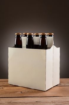 Closeup of a six pack of brown beer bottles on a rustic wooden table. Vertical format with a light to dark gray spot background.