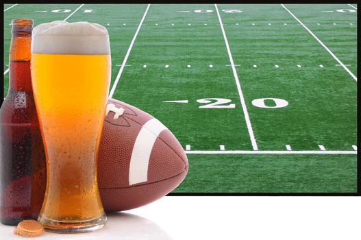 A frothy glass of beer with an American Football in front of a big screen television. Great for Super Bowl themed projects.