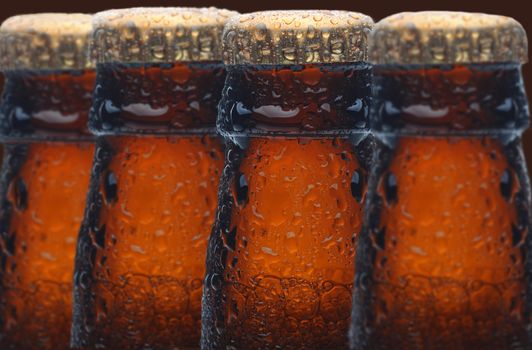 Closeup of four wet beer bottles with selective focus. The bottles only show the necks and caps and are covered with condensation.