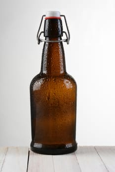 A swing top beer bottle against a light to dark background. The brown bottle is on a rustic whitewashed wood table. Vertical format with copy space.
