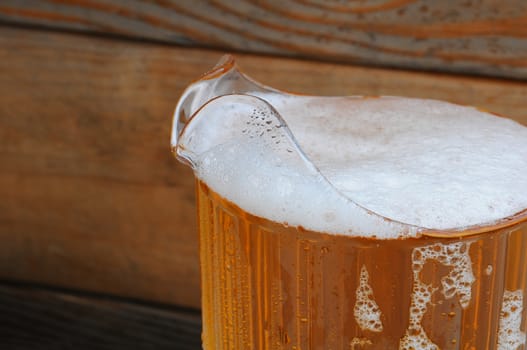 Closeup of a full pitcher of cold beer in front of a rustic wood background.