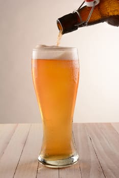 Beer pouring into a tall glass from a swing top bottle. On a wood table with a light ot dark background.