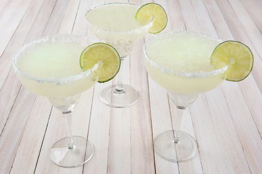 High angle view of three margarita cocktails on a rustic white wood table. Horizontal format.