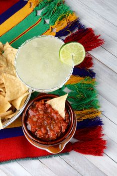 Cinco de Mayo Concept: Margaritas and Mexican food on a colorful  table cloth and wood table with chips and salsa.