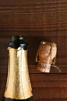 Top view of an opened Champagne bottle next to a cork and cage. Vertical format on dark wood background, with copy space.