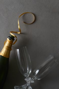 Champagne bottle with god ribbon and two glasses on a gray table.