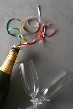 Champagne bottle with colorful ribbons and two glasses on a gray table.