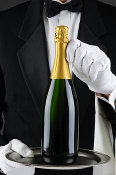 Closeup of a sommelier holding a champagne bottle on a serving tray in front of his torso. Man is wearing a tuxedo and is unrecognizable. Vertical Format.