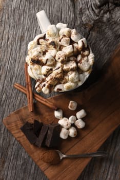 Overhead shot of a mug of hot cocoa with toasted marshmallows next to a cutting board with chocolate chunks and cinnamon sticks. Vertical Format - Shallow Depth of Field - Focus on the Mug.