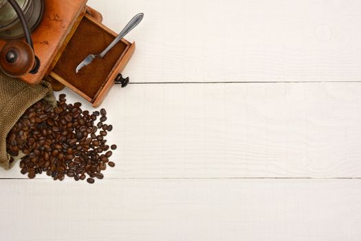 High angle shot of a bag of coffee beans and an antique  grinder on a rustic white wood table. The items are in the upper left corner leaving room for your copy.