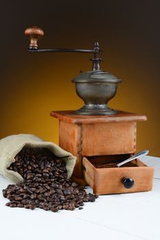 Coffee bean still life with antique grinder and spilled beans on a rustic wood table. Horizontal format with warm toned light to dark background..