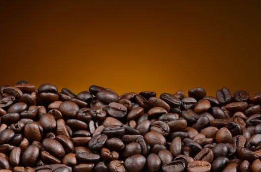 Closeup of fresh roasted coffee beans with a light to dark warm background. The beans fill the bottom of the frame, the top half is open for copy space.