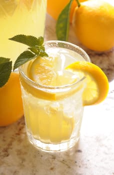 Close up of a Glass of Lemonade on counter in front of window with pitcher and lemons vertical format shallow DOF High angle