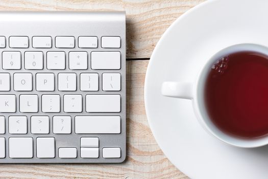 Closeup of a computer keyboard and cup of hot coffee on a white rustic table. High angle shot in horizontal format.