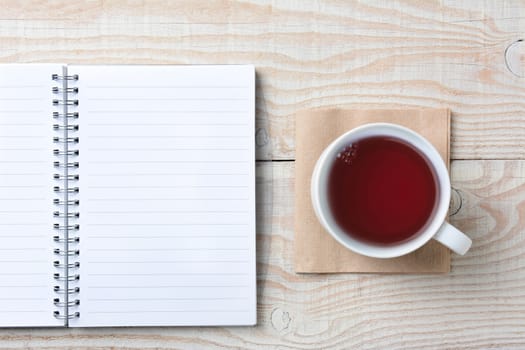 Closeup of an open notebook and a cup of hot tea on a rustic white wood table. High angle shot in horizontal format.