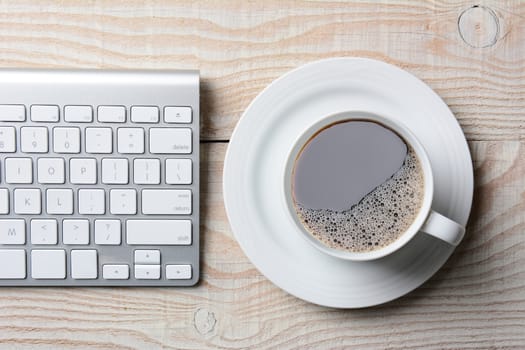 Computer keyboard and cup of hot coffee on a white rustic table. High angle shot in horizontal format.