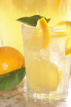 Close up of a Glass of Lemonade with pitcher and lemon behind vertical format shallow DOF