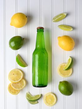 High angle shot of a bottle of lemon lime soda surrounded by fresh cut and whole lemons and limes. Vertical format. 