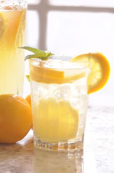 Close up of a Glass of Lemonade on counter in front of window with pitcher and lemons vertical format shallow DOF