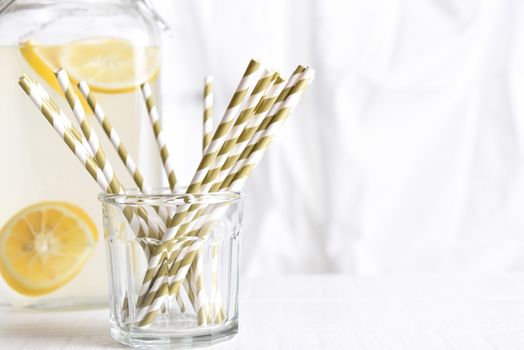 Summer Lemonade Still Life: A lemonade pitcher with a glass of drinking straws in front of a kitchen window. Horizontal format with copy space. Focus is on straws.