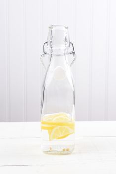 A swing top bottle with lemon water on a white wood table.